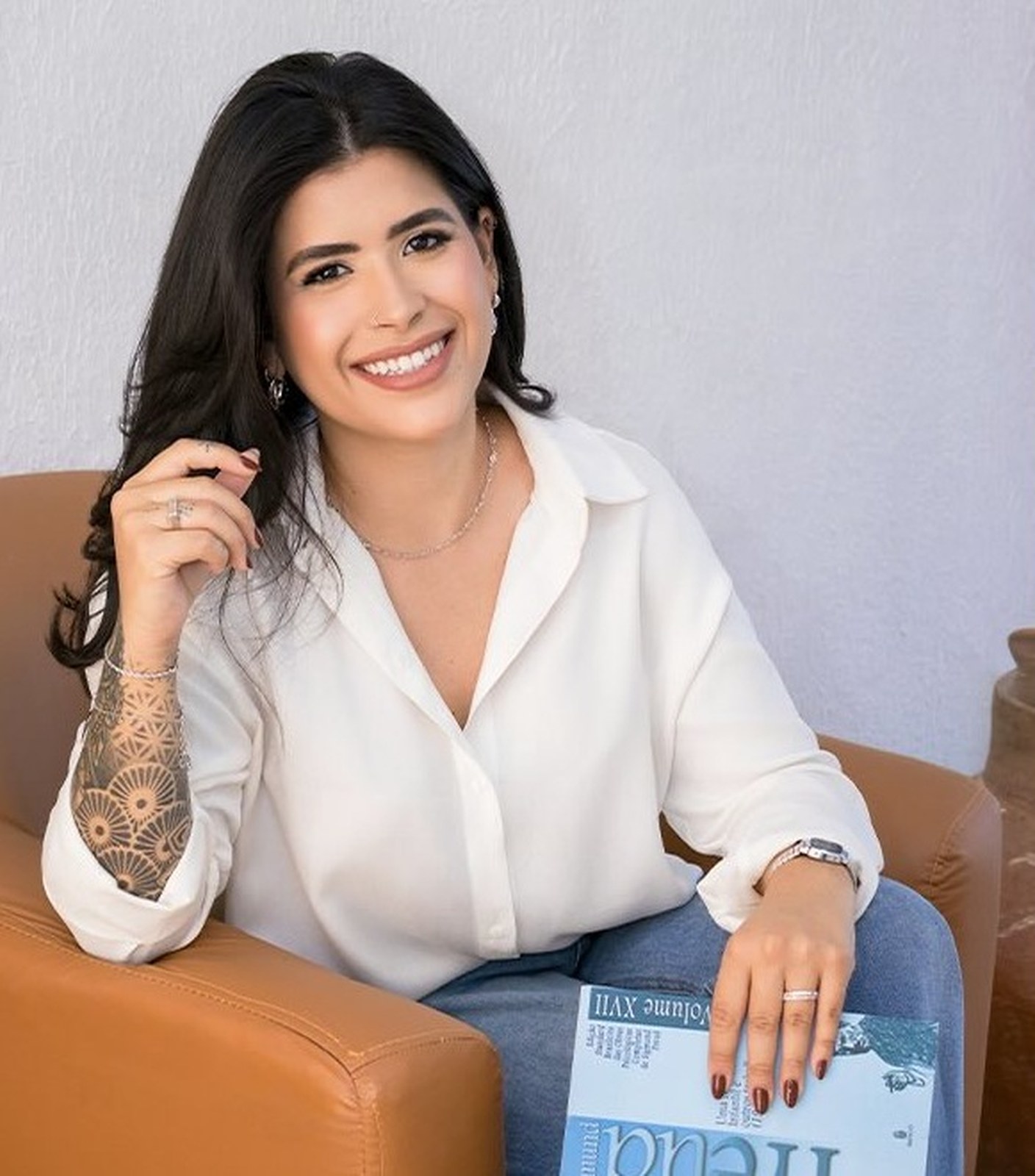 Fernanda sorrindo, sentada na poltrona com um livro no colo